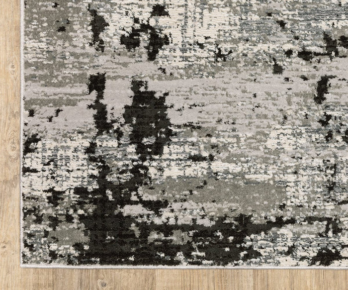 A close-up view of the Oriental Weavers Caravan 4153Q rug, showcasing its rectangular shape and abstract nature-inspired pattern in shades of gray, black, and white, positioned on a wooden floor. Crafted from space-dyed polyester, this design offers a textured and modern appearance.