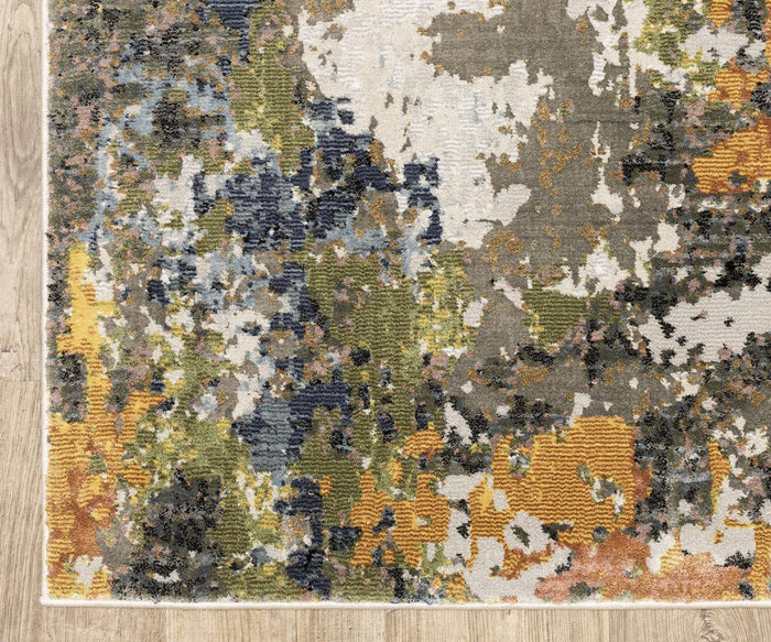 The Oriental Weavers Caravan / 502X Rug from the Caravan Collection showcases a nature-inspired, painterly pattern with splashes of green, blue, yellow, gray, and white tones on a wooden floor. Crafted from space-dyed polyester, this abstract area rug offers enhanced depth and visual interest.