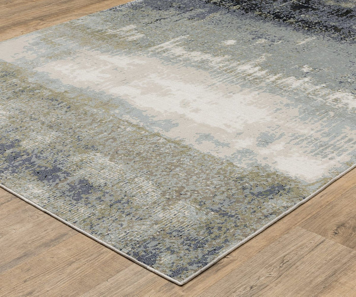 The Oriental Weavers Caravan 5571H Rug showcases abstract, nature-inspired patterns in blue, gray, cream, and beige tones on a wooden floor. Crafted from space-dyed polyester, this rug offers a textured, painterly effect that seamlessly blends the colors for a modern look.