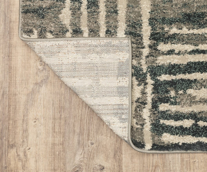A corner of the Oriental Weavers Carson / 745C Rug, featuring a gray and beige pattern, is folded over on a light wood floor to reveal its plush carpet underside and contrasting textures.