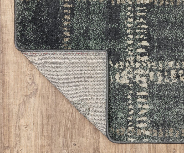 The Oriental Weavers Carson / 746J Rug is shown on a wooden floor with one corner turned up, highlighting its textured underside and stitched edge. Made from durable polypropylene, this rug offers a blend of modern style and lasting quality.