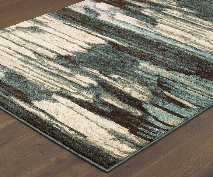 A close-up of the Oriental Weavers Carson / 9675A Rug on a wooden floor, showcasing an abstract pattern with cream, blue, and brown in streaks and irregular shapes. Crafted from durable polypropylene, this area rug is built to withstand everyday wear while bringing modern flair to your space.