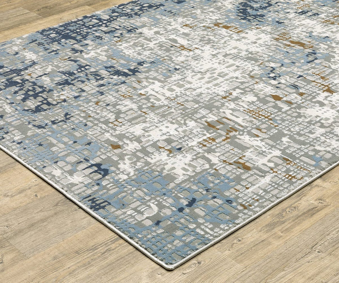 The Oriental Weavers Easton / 11E Rug is a rectangular area rug from the Easton Collection, featuring an abstract pattern in blue, gray, white, and gold tones against a light wood floor. Crafted using a durable power-loomed technique, this rug offers subtle texture and is finished with a thin light-colored border along the edges.