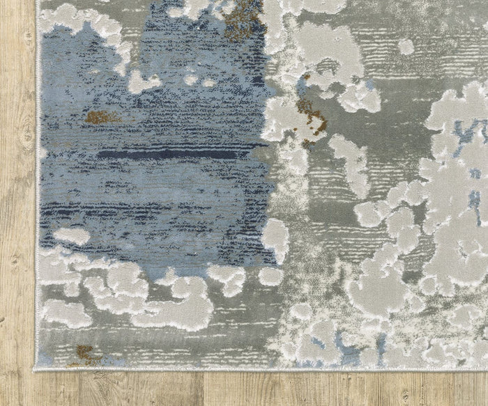 The Oriental Weavers Easton 4518X Rug from the Easton Collection features abstract patterns in blue, gray, and white tones with irregular shapes and patches. Displayed on a light wood floor, this durable power-loomed rug blends modern artistry with long-lasting quality.