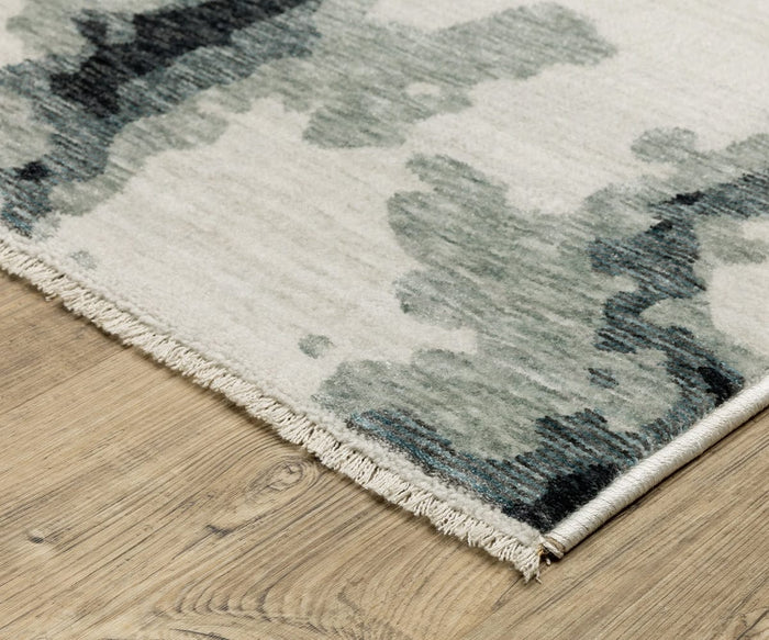 A close-up of the Oriental Weavers Echo / ECH08 Rug, power-loomed in Egypt, highlights its light-toned surface with abstract dark green and gray patterns resting on a wooden floor. Short fringe accents one edge of the rug.