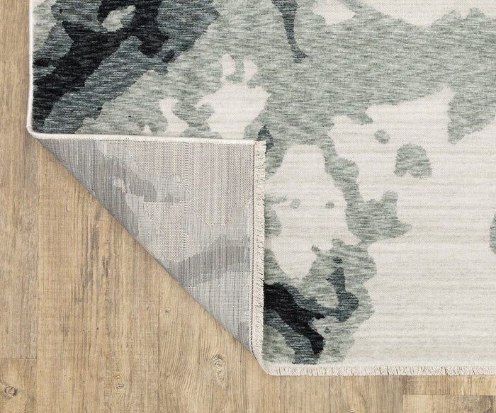 A corner of the gray and white patterned Oriental Weavers Echo / ECH08 Rug is flipped over on a wooden floor, revealing the rug’s underside and detailed stitching. This power-loomed rug is expertly crafted in Egypt, offering both style and durability.