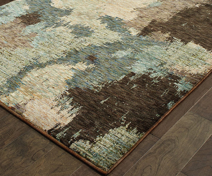 The Oriental Weavers Evolution / 8011B Rug from the Evolution Collection showcases an abstract design in shades of brown, beige, blue, and green over a wooden floor. Crafted from durable nylon for easy maintenance, this rug features a brushed painterly look with an irregular pattern and visible texture.