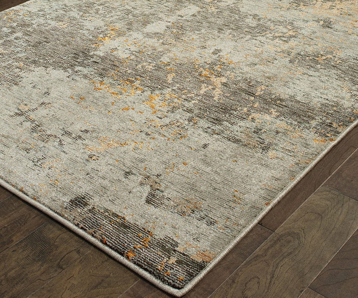 A close-up of the Oriental Weavers Evolution / 8025B Rug, a modern machine-woven piece from the Evolution Collection, showcasing an abstract gray and beige pattern accented with hints of gold and placed on a dark wooden floor. Crafted from durable nylon, this rug blends contemporary design with lasting quality.