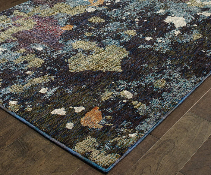 The Oriental Weavers Evolution / 8029A Rug from the Evolution Collection features a dark base accented with irregular, multicolored shapes in blue, beige, orange, and white tones. Made of durable nylon and machine-woven for lasting quality, only a corner of this rug is shown in the image, set on a wooden floor.