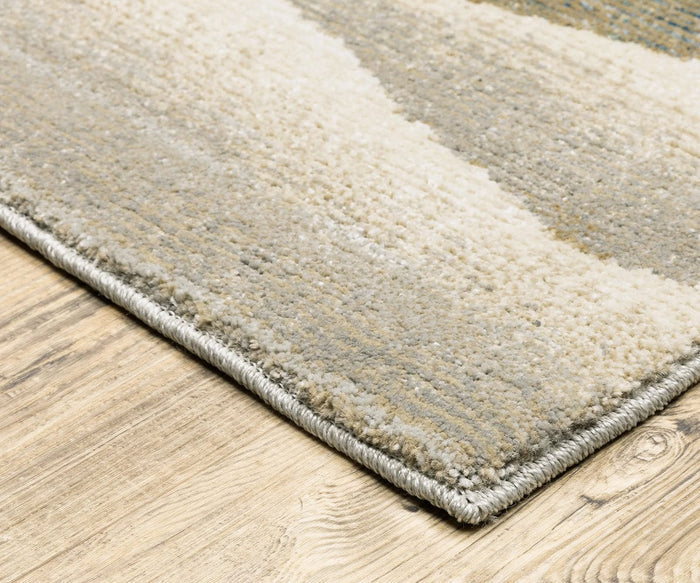 A close-up of the corner of the Oriental Weavers Evolution / 982C Rug reveals its beige and gray hues with subtle patterns, showcased on a light wood floor. Crafted from durable nylon, this rug features a soft, textured surface and neatly finished edges that are easy to maintain.