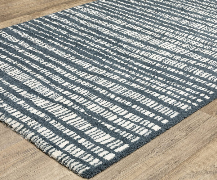 An Oriental Weavers Galileo GAL01 Rug from the Galileo Collection, featuring a blue and white abstract striped pattern, sits on a wooden floor. This microfiber polyester rug boasts a modern design with irregular horizontal lines and a dense pile for added comfort.