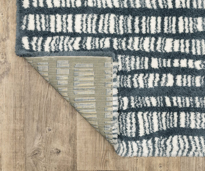 An Oriental Weavers Galileo GAL01 rug, featuring a blue and white pattern in microfiber polyester, rests on a wooden floor with one corner flipped to display its textured underside and dense pile.