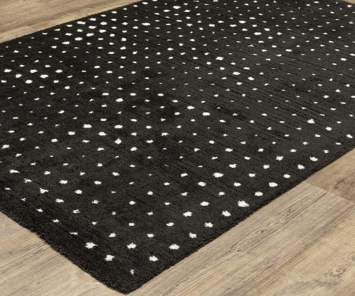 The Oriental Weavers Galileo / GAL04 Rug, showcasing a contemporary black base with scattered white polka dots, rests atop a light wood floor. This plush microfiber rug enhances any space with its blend of style and comfort.