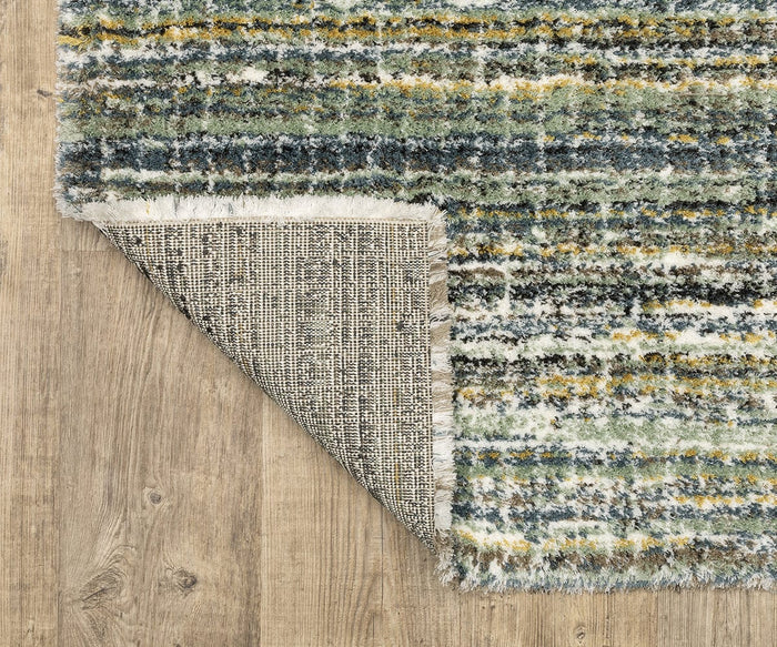 The Oriental Weavers Galileo / GAL07 Rug, featuring vibrant blue, green, yellow, and white stripes and a textured design, is shown partially flipped to display its beige woven underside on a light wood floor; crafted as a dense pile rug from soft microfiber polyester for enhanced comfort and durability.