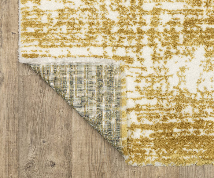 The Oriental Weavers Galileo / GAL10 Rug, featuring a white and yellow contemporary pattern, lies on a wooden floor with one corner flipped over to show its textured backing. Crafted from plush, dense pile microfiber polyester, this rug adds both comfort and style to any space.