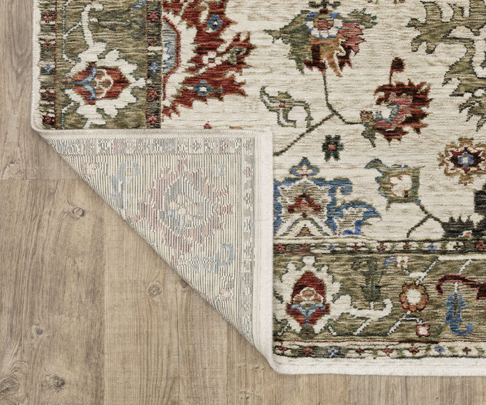 A corner of the Oriental Weavers Hastings / HA03W Rug is flipped over on a wooden floor, revealing the rug’s detailed underside and ornate floral designs in red, blue, and green tones on a beige background. The space-dyed polyester construction showcases intricate craftsmanship and vibrant patterns throughout.