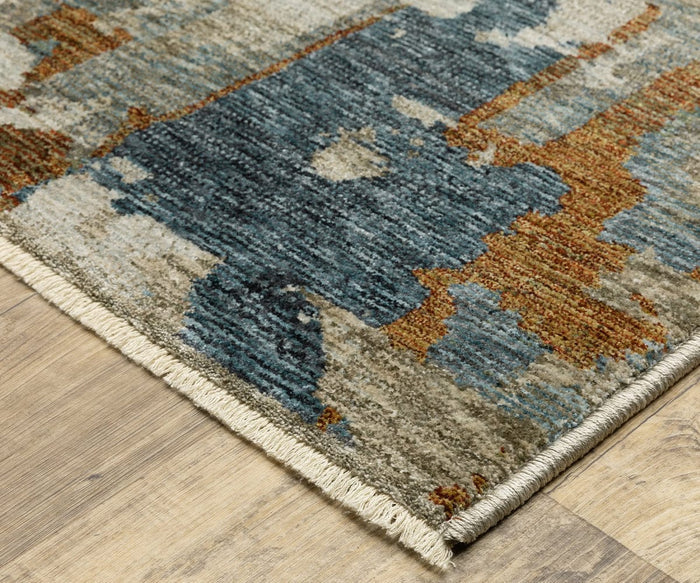 A close-up of the Oriental Weavers Hayden / HAY02 Rug, a space-dyed polyester rug in multicolored blue, beige, gray, and rust tones with abstract patterns and beige fringe along the edge, displayed on a light wood floor.