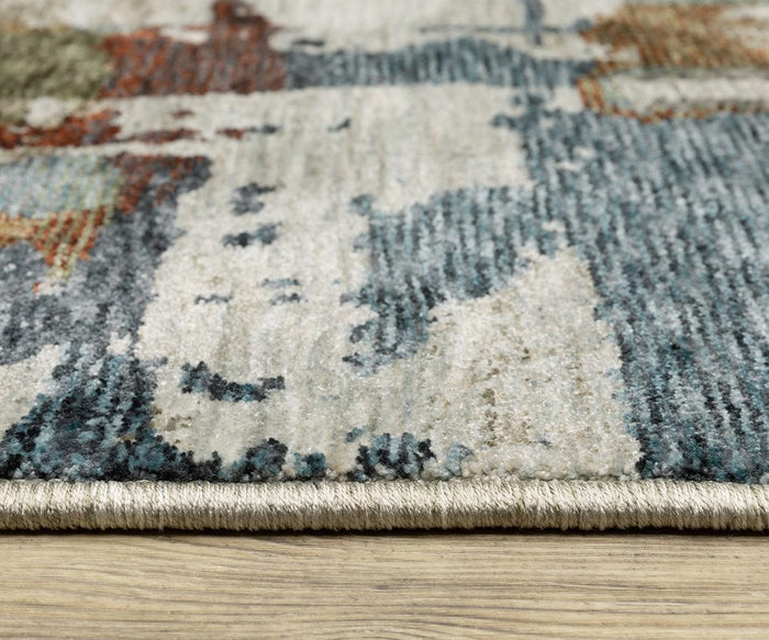 Close-up of the Oriental Weavers Hayden / HAY02 Rug, an abstract design featuring multicolored patterns in blues, creams, and browns. This space-dyed polyester rug showcases rich texture and detailed edging, beautifully displayed on a light wood floor.