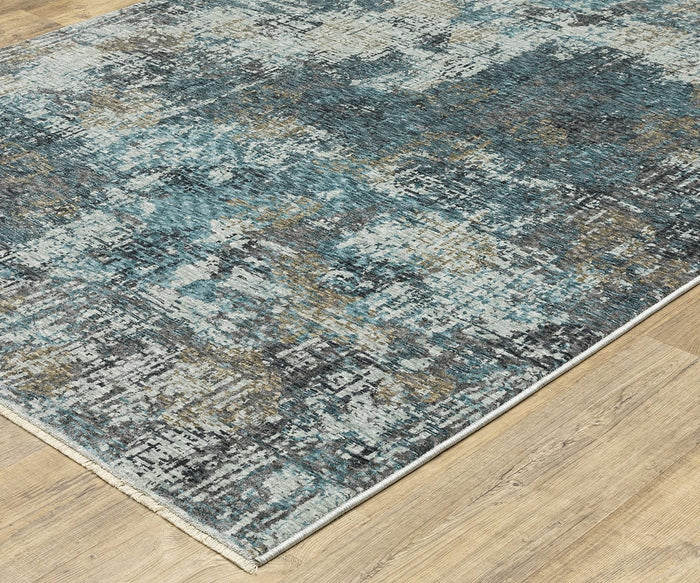 A blue, gray, and beige abstract design Oriental Weavers Hayden HAY03 Rug with a distressed pattern lies on a light wood floor. The rug’s corner is slightly shown, highlighting its textured surface and modern space-dyed polyester construction for a contemporary look.