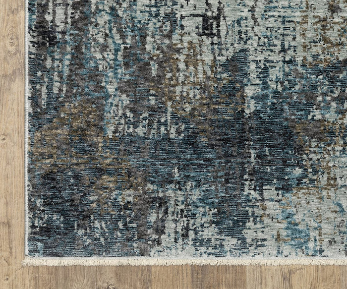 A close-up of the Oriental Weavers Hayden HAY03 Rug, a rectangular area rug showcasing a distressed blue, gray, and beige abstract pattern with fringes along one edge, placed on a light wood floor. Crafted from space-dyed polyester, this rug offers a unique and contemporary look.