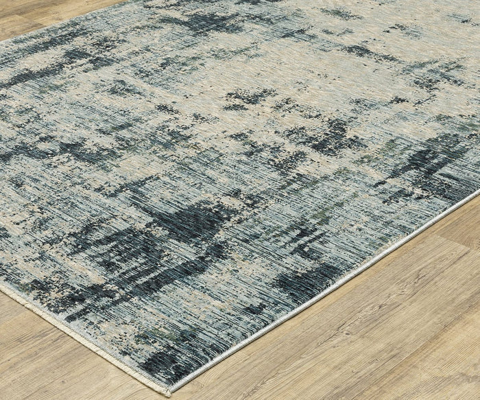 Oriental Weavers Hayden HAY04 Rug, featuring an abstract pattern in blue, gray, and beige tones, is showcased on a light wood floor. Crafted from space-dyed polyester, this rug offers a soft feel with finished edges and displays a textured, distressed appearance.