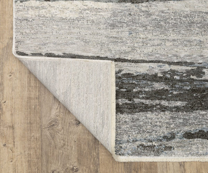 An Oriental Weavers Hayden / HAY07 Rug in gray and black, featuring a flipped corner that reveals its underside, rests on a light wood floor. This rug showcases an abstract design and is crafted from soft, space-dyed polyester for exceptional style and durability.