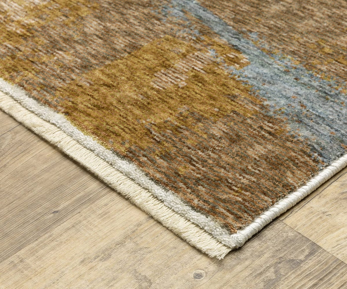 A close-up of a corner of the Oriental Weavers Hayden / HAY09 Rug with beige fringe, displayed on a light wood floor. This space-dyed polyester rug features an abstract pattern in shades of brown, gold, and blue.