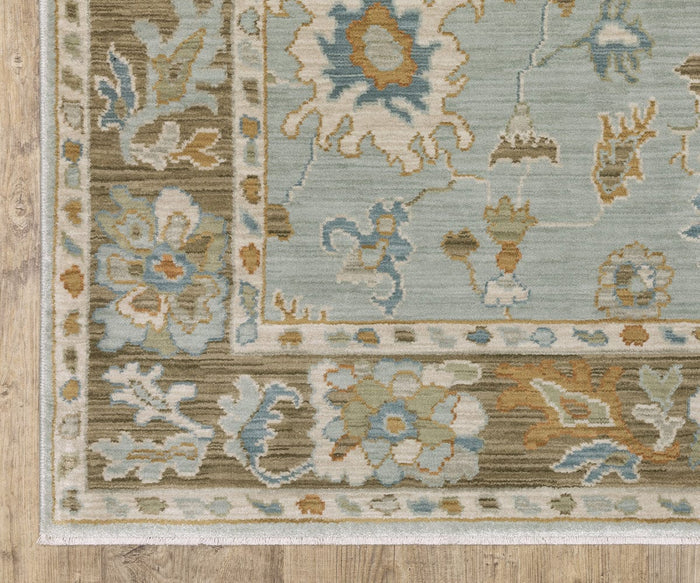 A corner of the Oriental Weavers Maeve / MAE06 Rug, featuring Persian-inspired floral and geometric designs in blue, beige, green, and brown hues on a wooden floor. This rug boasts a decorative border and a soft, textured appearance, expertly crafted from space dyed polypropylene for enhanced durability.