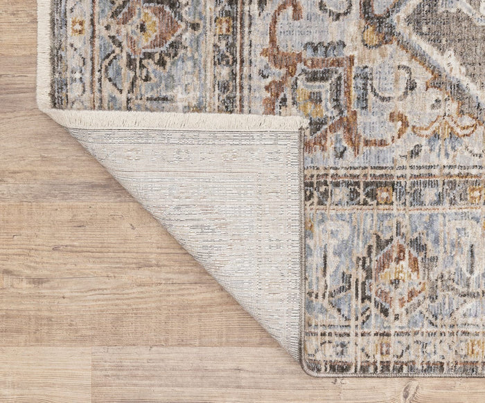 A corner of the Oriental Weavers Maharaja / 1803X Rug on a wooden floor is flipped over, revealing the rug’s underside. This Persian-inspired rug features blue, beige, and gold tones in a traditional design.