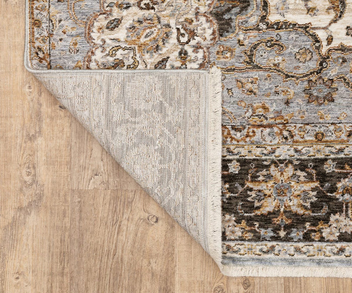 Corner of the Oriental Weavers Maharaja / 660J Rug from the Maharaja Collection, featuring ornate, traditional designs in blue, beige, and brown hues, shown on a wooden floor. The corner is flipped to reveal the rug’s durable polyester underside.