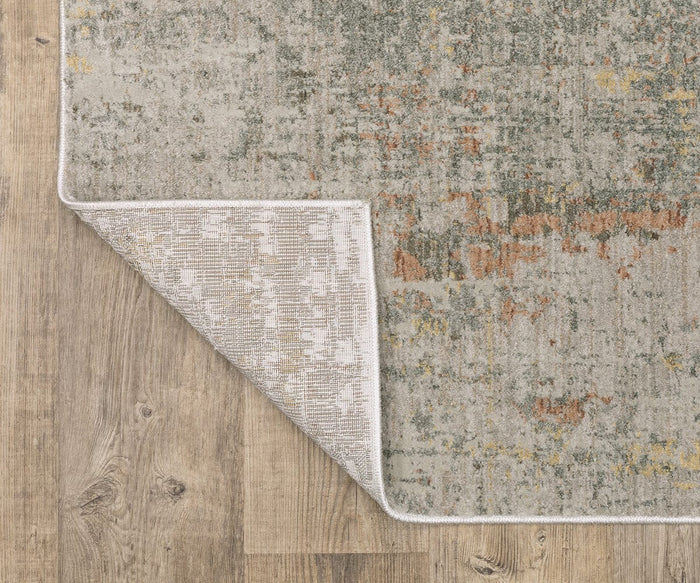 A close-up of the rectangular Oriental Weavers Mallory / MAL05 Rug on a wooden floor, with one corner flipped to display the underside pattern. Crafted from space-dyed polypropylene, this rug showcases earthy shades with a distressed, multicolored design in beige, green, and orange tones.