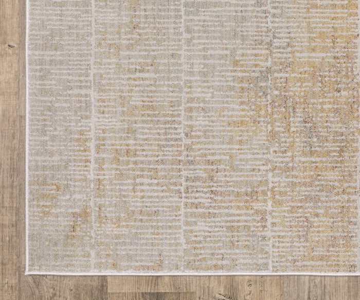 A close-up of the Oriental Weavers Mallory / MAL09 Rug, featuring a subtle beige and gold abstract pattern, power-loomed in space dyed polypropylene, shown on a wooden floor. The rug’s rectangular edge and part of its border are visible in the image.