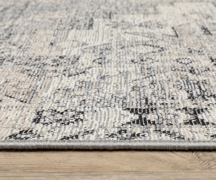 Close-up view of the edge of the Oriental Weavers Naples / 1346Z Rug, showcasing its textured polypropylene surface and neutral color palette with light gray, beige, and black patterns, placed on a light wooden floor.