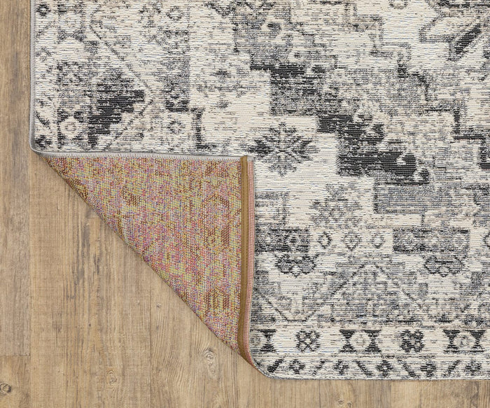 A patterned Oriental Weavers Naples / 1346Z Rug with one corner flipped over, revealing a colorful underside. Featuring black, white, and gray geometric designs, this rug is placed on a light wood floor and serves as a stylish indoor-outdoor option.