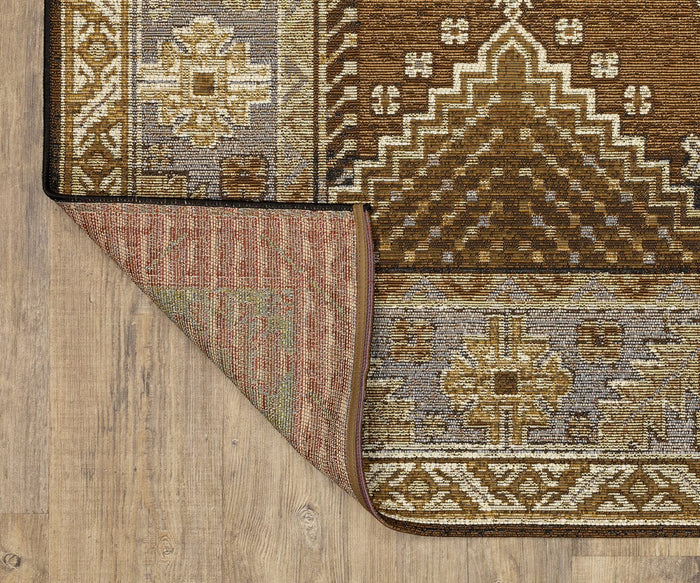 The Oriental Weavers Naples / 1441X Rug, featuring brown, gold, and gray geometric and floral patterns in fade-resistant polypropylene, lies on a wooden floor. One corner of the rug is folded over to reveal an alternate pattern on the underside.