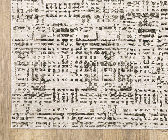 A corner of the Oriental Weavers Nebulous / 2060W Rug, showcasing its modern geometric black and beige pattern woven from soft polyester yarn, is placed on a light wooden floor—an ideal representation of contemporary abstract rugs.