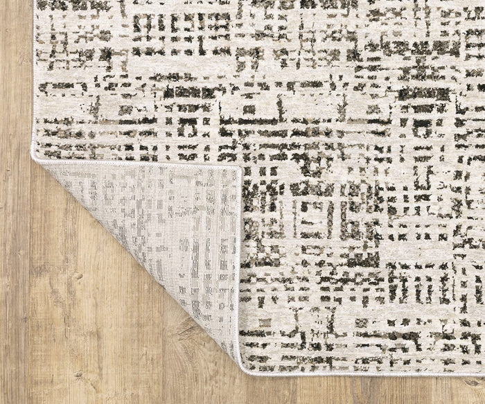The Oriental Weavers Nebulous / 2060W Rug, featuring a beige and gray abstract pattern and crafted from polyester yarn, is shown with one corner flipped to display its underside. This modern rug from the Nebulous Collection is placed on a light wood floor.