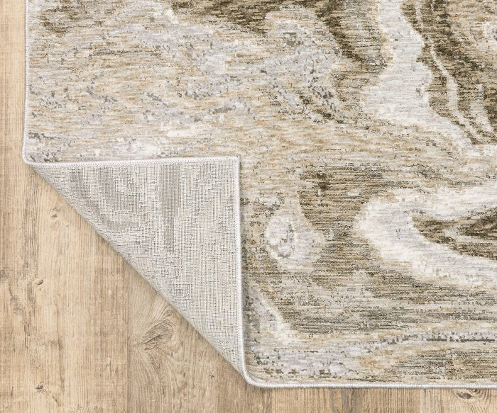 The Oriental Weavers Nebulous / 530E Rug, featuring a beige and gray marbled pattern, is displayed on a wooden floor. One corner of this modern abstract rug is flipped over to show its non-slip backing and soft polyester yarn construction.