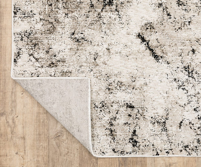 A corner of the Oriental Weavers Nebulous / 561E Rug, featuring a distressed gray and black pattern on a light background, is folded over to show the underside. Woven from soft polyester yarn, this modern abstract rug rests gracefully on a wooden floor.
