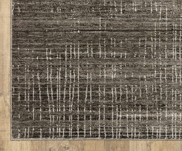 A close-up of the Oriental Weavers Nebulous / 751D Rug reveals its gray and black patterned design, highlighted by vertical and horizontal white lines. Placed on a light-colored wooden floor, this modern abstract rug from the Nebulous Collection is crafted from space-dyed polyester, enhancing its unique texture and contemporary appeal.