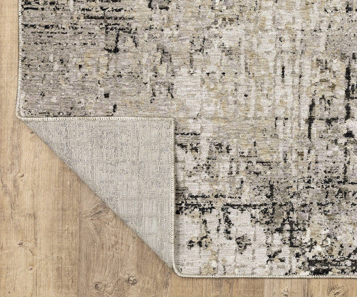 A corner of the Oriental Weavers Nebulous / 91D Rug is flipped over on a wooden floor, revealing both the modern abstract rug’s patterned front and its woven back, crafted from soft polyester yarn.