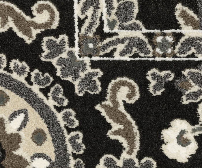 Close-up of the Oriental Weavers Raylan / RAY05 Rug, displaying black, white, gray, and brown tones with ornate swirling designs and a rectangular border overlapping a circular motif. Subtle Persian-inspired patterns and geometric accents are highlighted by its high/low construction, adding texture and visual interest.