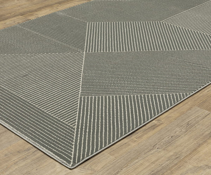 An Oriental Weavers Raylan / RAY08 Rug in gray, featuring a modern geometric motif of diagonal white lines and intersecting shapes, is placed on a light wood floor. Its fade-resistant material ensures the design’s lasting vibrancy.