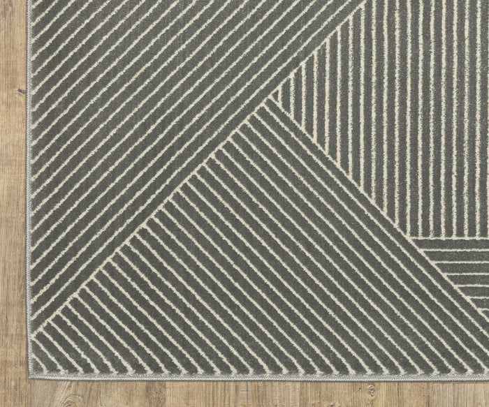 A close-up of the Oriental Weavers Raylan / RAY08 Rug highlights its striking geometric motif, featuring diagonal white lines on a dark gray background, set atop a light brown wooden floor. This fade-resistant area rug combines style and durability, making it an ideal choice for any modern space.