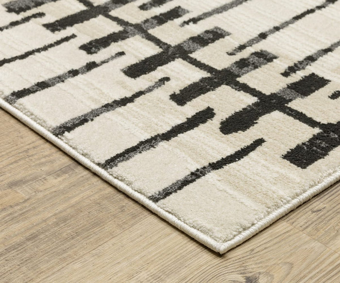 A close-up of the Oriental Weavers Raylan / RAY11 Rug, showcasing its fade-resistant beige surface adorned with striking black geometric motifs, displayed beautifully on a wooden floor.