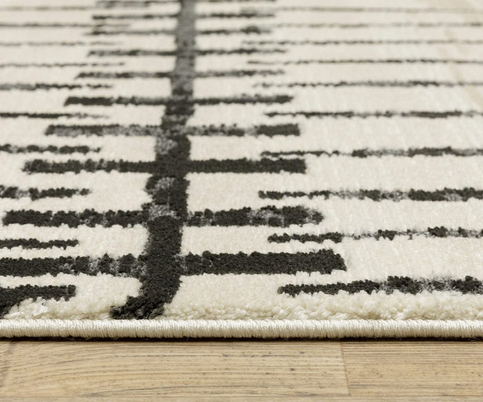 Close-up of the Oriental Weavers Raylan / RAY11 Rug in beige and black, featuring a modern geometric motif with a linear pattern, displayed on a light wooden floor. The fade-resistant edge and textured surface of the rug are clearly visible.