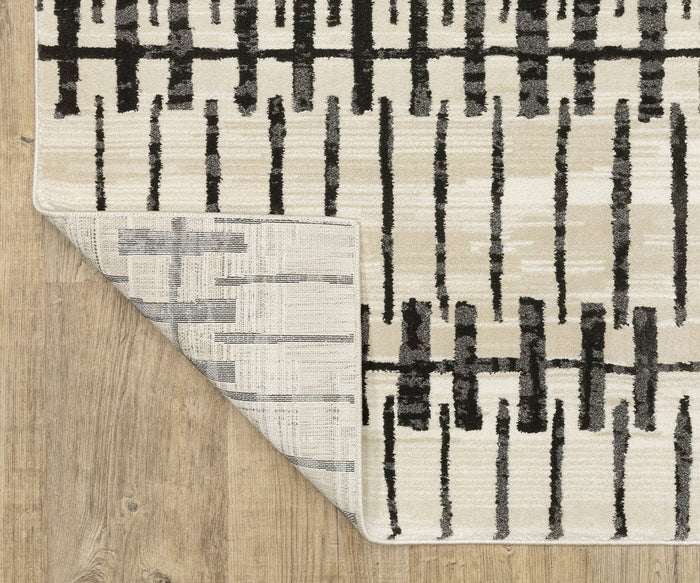 An Oriental Weavers Raylan / RAY11 Rug in beige and black, featuring an abstract linear pattern, is displayed on a wooden floor. The flipped corner reveals the underside’s lighter, muted geometric motif. This fade-resistant rug seamlessly blends style and durability.