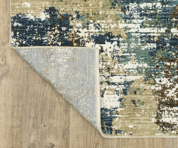 The Oriental Weavers Reed / RE06A Rug, featuring a modern abstract pattern in blue, green, beige, and white hues, is displayed on a wooden floor. One corner of the textured rug is flipped to reveal its gray underside made from space-dyed polypropylene.