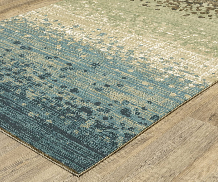A rectangular Oriental Weavers Reed / RE08A Rug with a super-soft feel, showcasing a gradient design that transitions from teal to beige and is accented with scattered dot patterns, placed on a light wood floor.
