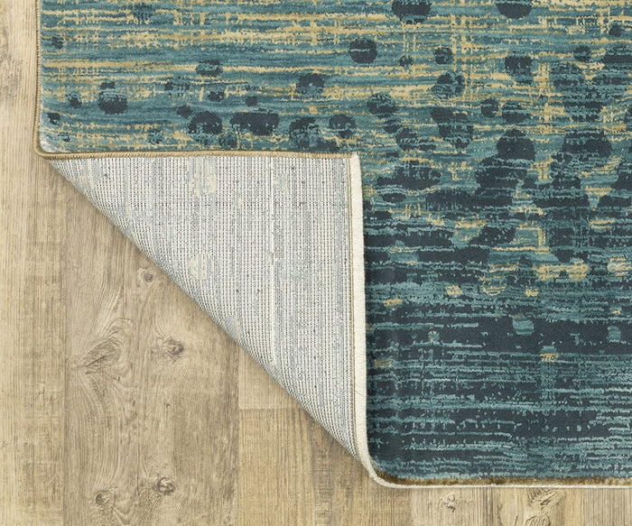 The Oriental Weavers Reed / RE08A Rug, featuring a blue and gold modern abstract pattern, is displayed on a wooden floor with one corner turned over to show its light-colored underside.